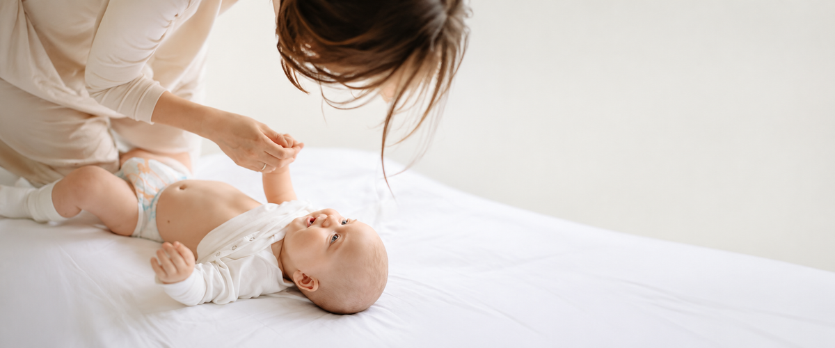 Mother changing diaper of smiling baby on white surface