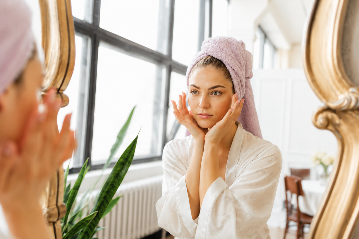 Woman examining glowing skin in mirror after facial