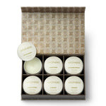 A set of white candle jars and two round lids arranged in front of a decorative patterned box