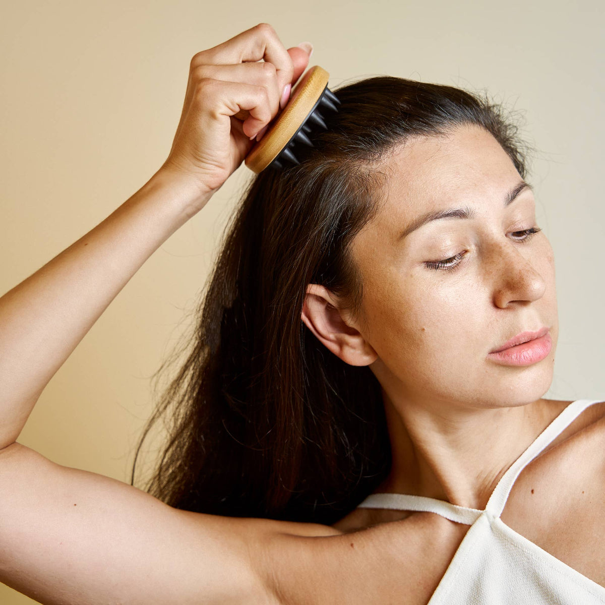 Woman brushing her hair with a wooden brush against a beige background