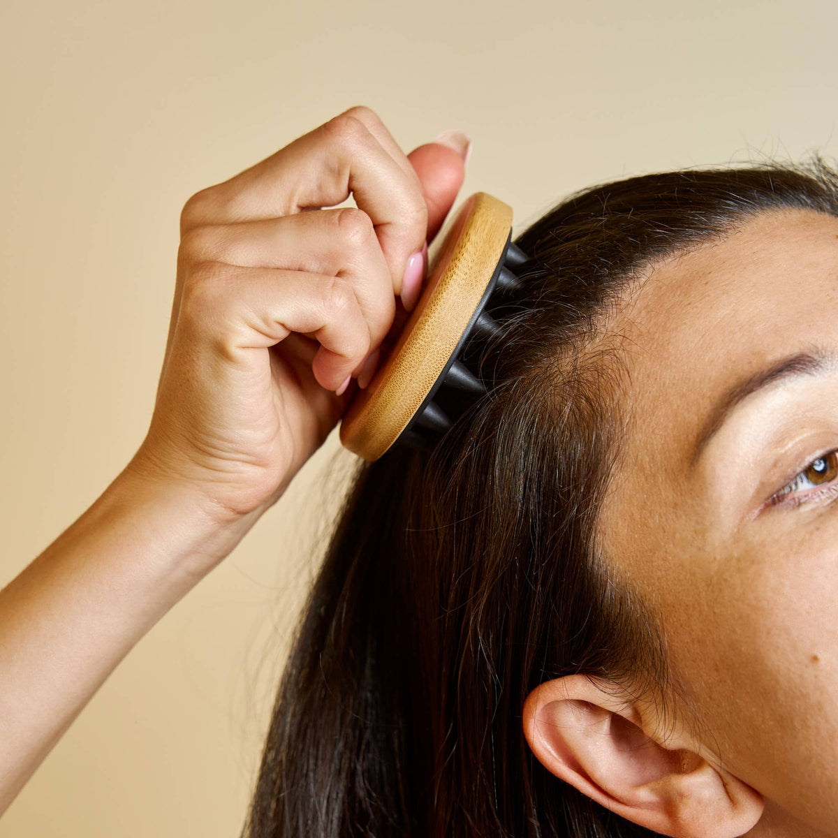 Person using a wooden hairbrush on their head against a beige background