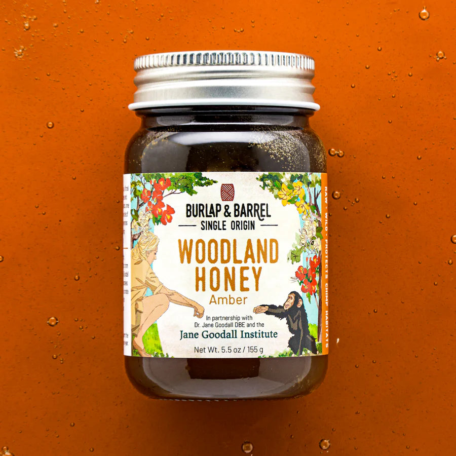 Burlap & Barrel Single Origin Woodland Honey Amber glass jar on a warm orange background with honey droplets, Jane Goodall Institute partnership, 5.5oz