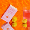 Cheeky Bonsai Bye Bye UTI Urinary Tract Support Hibiscus Lemonade health drink mix lifestyle photo with lemon slices and pink drink on vibrant orange background