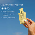 Cymbiotika Liposomal Vitamin D3 K2 CoQ10 Tangerine lifestyle ad - hand holding yellow pouch against blue sky, Liquid sunshine in a packet, supports immune health, calcium regulation, cellular energy