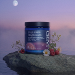 A blue jar of Deep Calm Magnesium+ supplement sits on a rock in calm water at sunset, with flowers, raspberries, and a moon in the background.