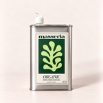 A rectangular metal can of Masseria Organic Extra Virgin Olive Oil with a white spout cap, featuring a green and white label, set against a solid light beige background.