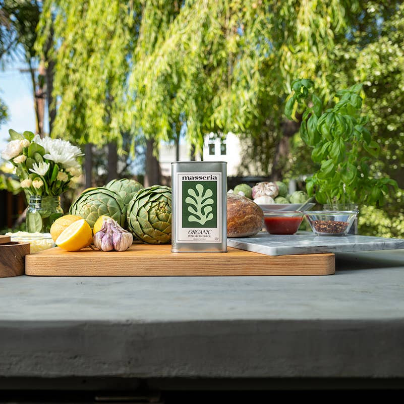 Table with fresh produce and a bottle of olive oil in an outdoor setting