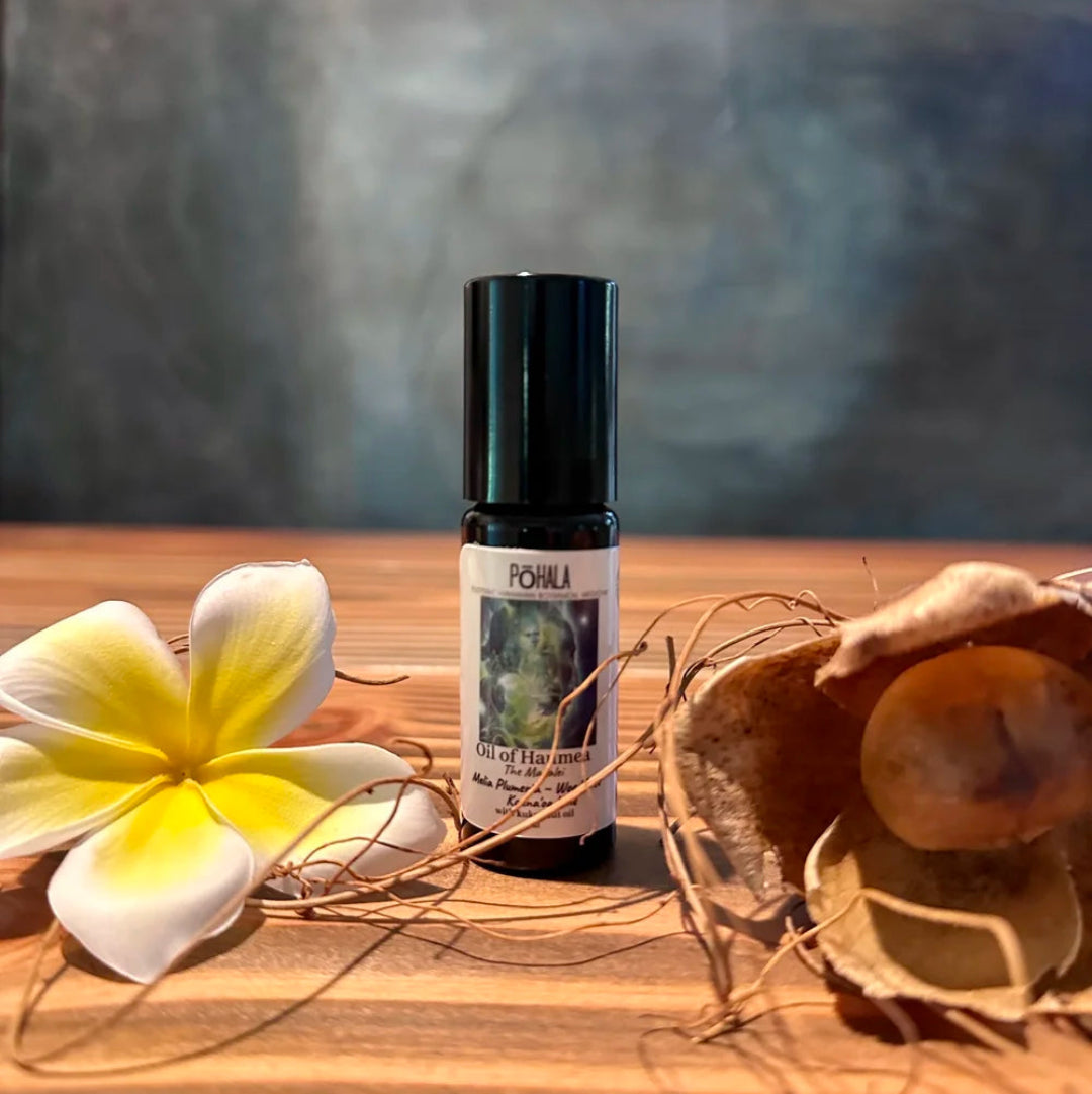 Pohala Oil of Haumea roll-on bottle lifestyle photo with plumeria flowers and coconut shell on a wooden surface with blue background