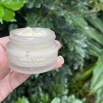 Hand holding a jar of 'athar'a pure' eye cream against a green leafy background