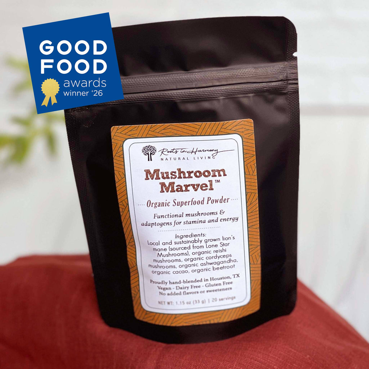 A stand-up pouch of Mushroom Marvel Organic Superfood Powder by Roots to Harmony Natural Living, shown on a red fabric surface with a blue Good Food Awards 2026 badge in the top left corner.