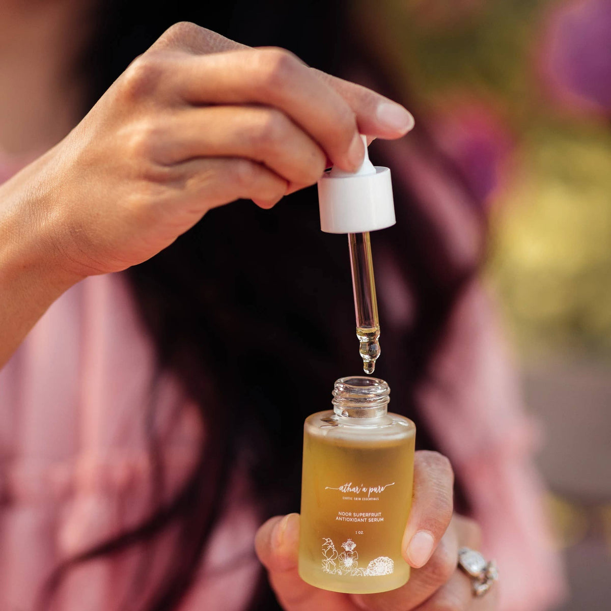 A close-up of a person holding a small glass bottle filled with golden-yellow liquid and lifting a white dropper above it