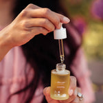 A close-up of a person holding a small glass bottle filled with golden-yellow liquid and lifting a white dropper above it