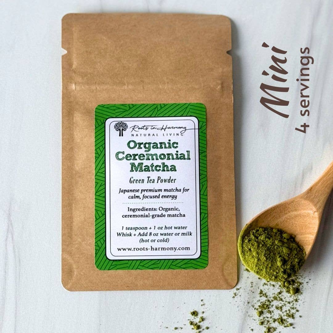 A kraft paper pouch of Roots of Harmony Natural Living Organic Ceremonial Matcha green tea powder, shown on a white wood background with a wooden spoon holding matcha powder and the text 'Mini 4 servings'.