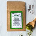 A kraft paper pouch of Roots of Harmony Natural Living Organic Ceremonial Matcha green tea powder, shown on a white wood background with a wooden spoon holding matcha powder and the text 'Mini 4 servings'.