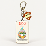 A rectangular metal tin keychain with a hanger and a small monkey charm, branded 'WOO - world of woo'. The tin is labeled 'PINEAPPLE SOLID OIL BALM' and features a colorful illustrated droplet on a cream background, set against a plain white studio background.