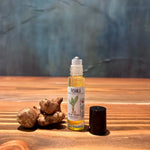 Pohala Oil of Olena Turmeric roll-on bottle displayed alongside fresh turmeric roots on a wooden surface with blue-grey background