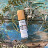 Pohala Lua Trifecta Oil roll-on bottle with bamboo cap surrounded by dried botanical plants on a rustic blue-painted wooden surface