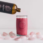 Bottle of 'Pure Rose' rose water being poured into a glass with pink stones and a white background.