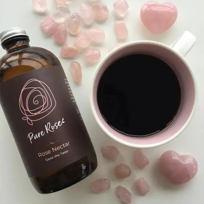 Bottle of Pure Rose' Rose Nectar next to a cup of coffee and pink stones on a light surface