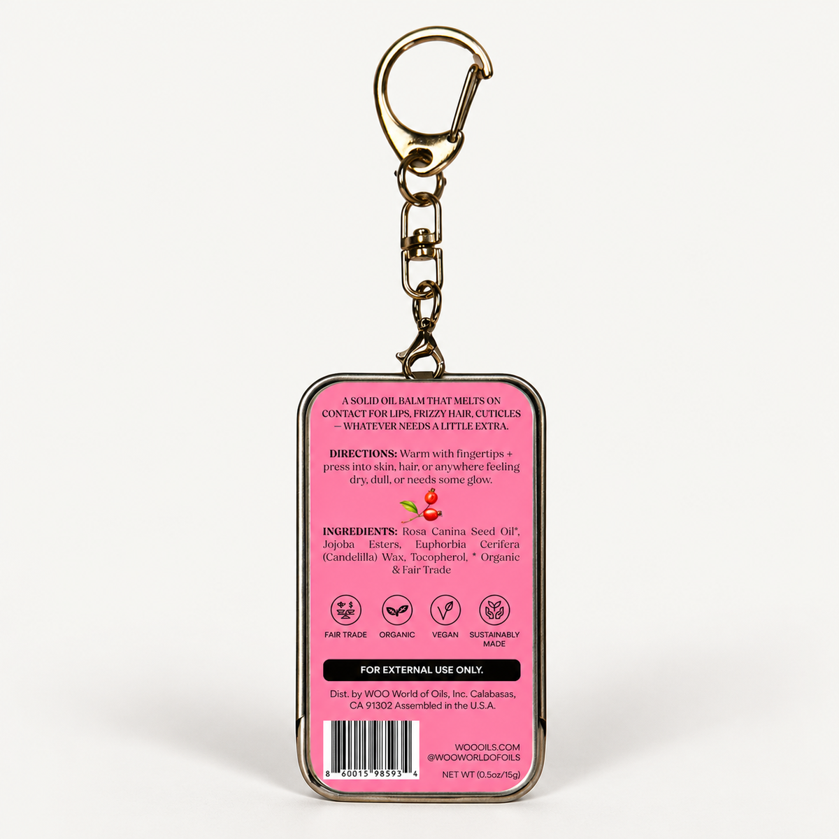 A rectangular keychain with a pink back panel showing product instructions, ingredients, and a barcode, attached to a gold-tone metal key ring and clasp, on a plain white background.